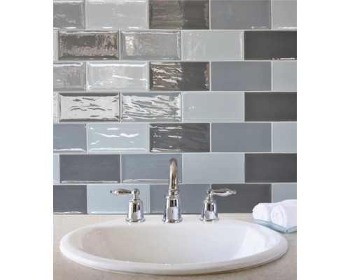 Waschbecken mit Armatur und Fliesen in Grau- und Blautönen im Badezimmer.