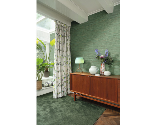 Wohnzimmer mit grüner Textiltapete, Teppich, Vorhängen und Holzkommode