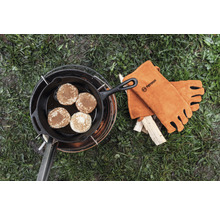 Pfannkuchen in einer gusseisernen Pfanne auf einem Kochgestell mit Petromax Logo Lederhandschuhen neben Holz.