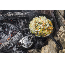 Gusseisenpfanne mit Reis und Gemüse am Lagerfeuer mit Teekessel