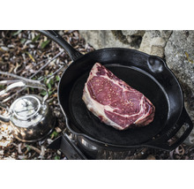Ein rohes Steak in einer gusseisernen Bratpfanne auf einem Kocher mit einem Wasserkessel daneben