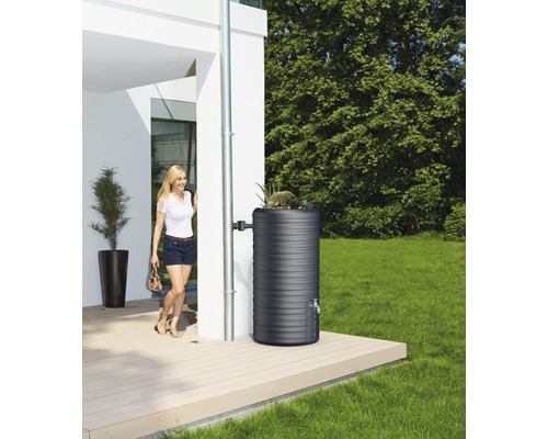 Regentonne im Garten neben einem Haus mit einer Frau