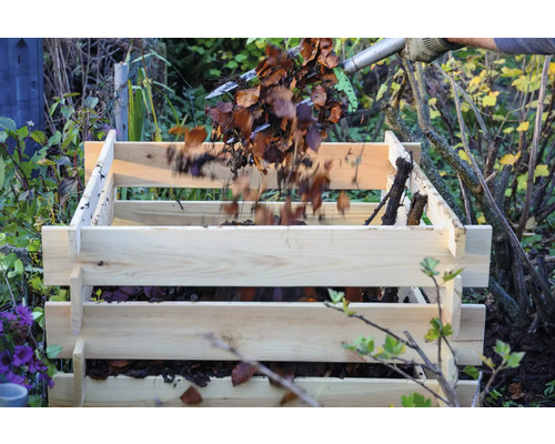 Befüllen eines Holzkomposters mit Laub und Gartenabfällen.