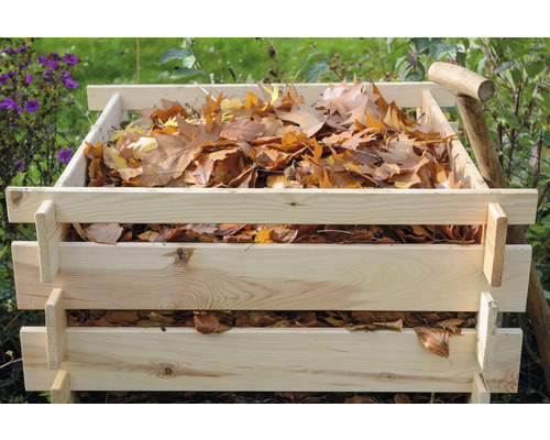 Holzkomposter gefüllt mit Laub und einem Spaten im Garten.