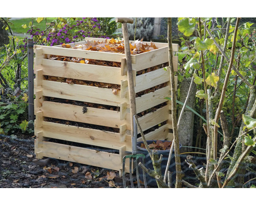 Holzkomposter mit Herbstlaub und einer Mistgabel im Garten.