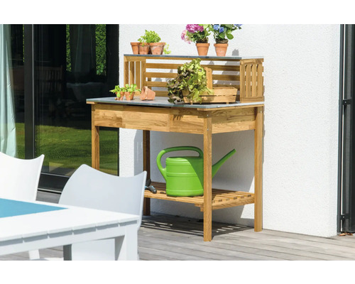 Gartenszene mit einem hölzernen Pflanztisch, Pflanzen und einer Gießkanne