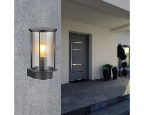 Eine schwarze Wandleuchte mit klarem Glas an einer Hauswand neben einer Haustür.