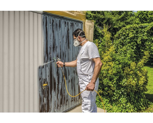 Mann lackiert Garagentor mit Farbspritzgerät. Heimwerken im Garten.