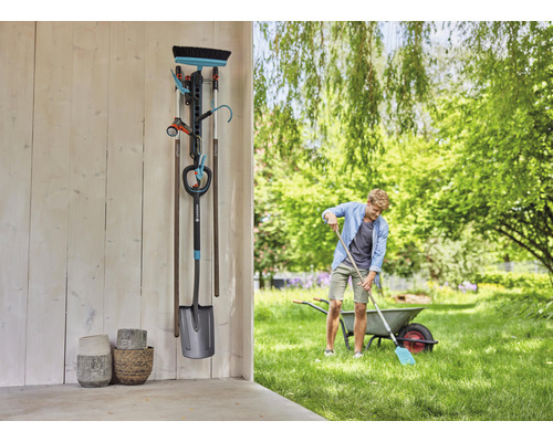 Gartenszene mit Gerätehalter, Gartengeräten und Person, die im Garten arbeitet