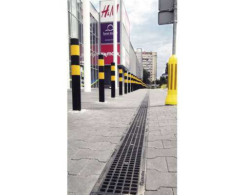 Außenaufnahme mit Entwässerungsrinne und Absperrpfosten vor einem Einkaufszentrum.