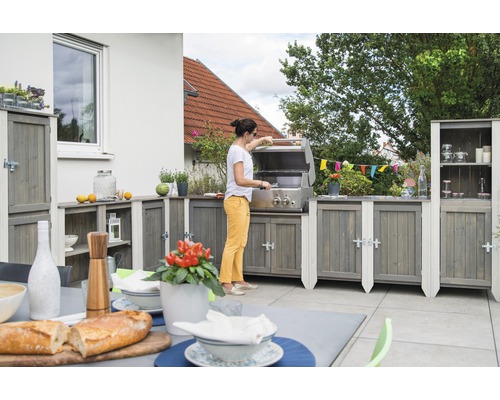 Outdoor-Küche mit Grill, Schränken und Tischgedeck auf einer Terrasse