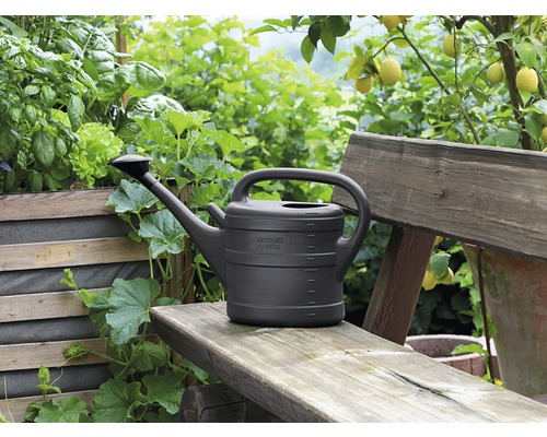 Gießkanne aus Kunststoff auf einer Holzbank im Garten