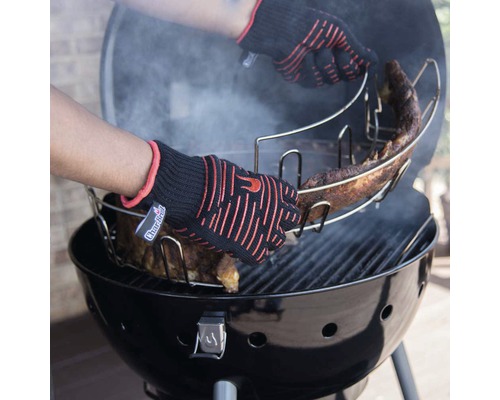 Person mit Grillhandschuhen platziert Rippchenhalter mit Rippchen auf Holzkohlegrill