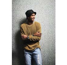 Mann mit Hut, Pullover und Jeans steht vor einer Wand