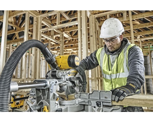 Ein Mann mit Schutzhelm und Sicherheitsweste bedient eine DeWalt Kapp- und Gehrungssäge in einer Rohbaukonstruktion.