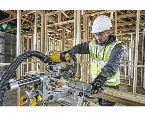 Ein Arbeiter benutzt eine Kapp- und Gehrungssäge von DeWalt auf einer Baustelle, um ein Holzbrett zu schneiden.