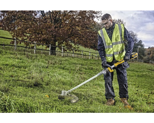 Eine Person trimmt Gras mit einem Akku-Rasentrimmer im Freien.