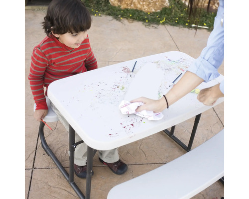 Kind malt am Tisch und eine Person wischt die Oberfläche ab