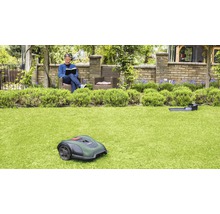 Ein Mann liest in seinem Garten, während ein Rasenmähroboter das Gras mäht.