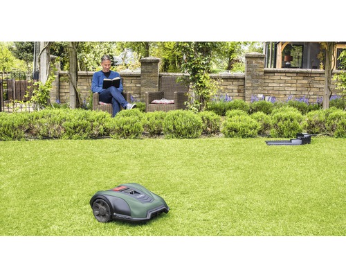 Ein Mann liest in seinem Garten, während ein Rasenmähroboter das Gras mäht.