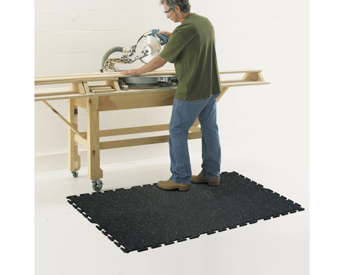 Eine Person bedient eine Kappsäge auf einem Arbeitstisch, stehend auf einer schwarzen Werkstattmatte.