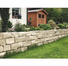 Gartenmauer aus Natursteinen mit Haus und Gartenhaus im Hintergrund