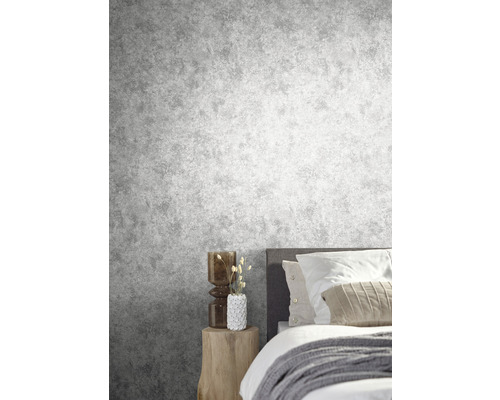 Schlafzimmer mit grauer Betonoptik-Tapete, Bett und Beistelltisch aus Holz.