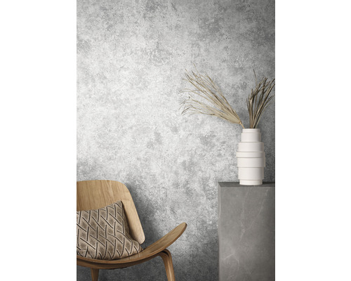 Szene mit Holzstuhl, Kissen, Vase und dekorativen Zweigen vor einer grauen Wand