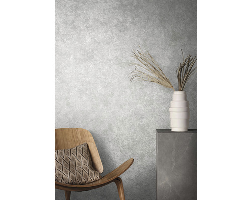 Dekoratives Interieur mit Stuhl, Kissen, Vase und Zierpflanzen vor einer strukturierten Wand