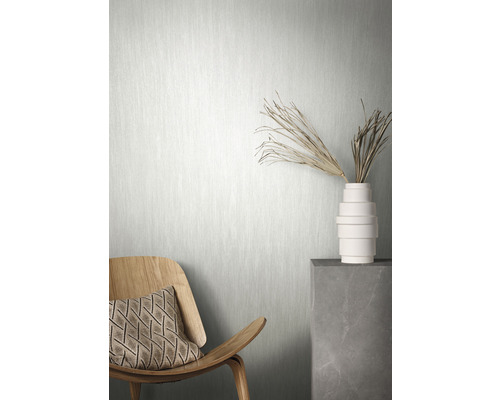 Szene mit einer hellen Vliestapete, einem Holzsessel mit Kissen und einer Vase mit Dekoration auf einem Sockel