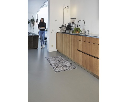 Heller Raum mit Küchenzeile und einer Frau mit einem Teller und einem Teppich auf dem Boden.