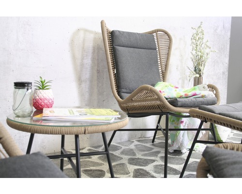 Szene mit Rattansessel, grauem Kissen und Beistelltisch mit Glasplatte