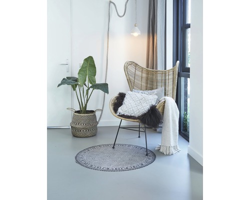 Helles Interieur mit Rattansessel, Pflanze im Korb, rundem Teppich, Kissen und Tagesdecke