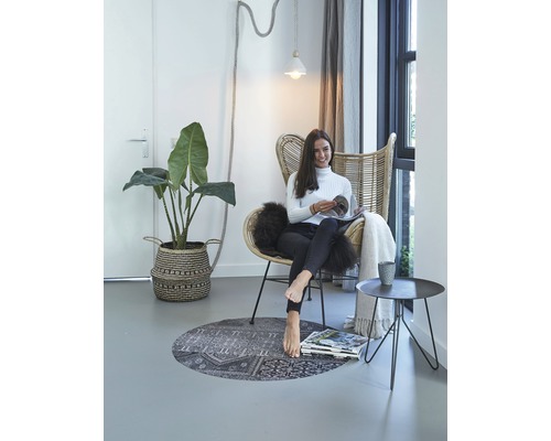 Helle Inneneinrichtung mit Rattansessel, Pflanze, Teppich und lesender Frau