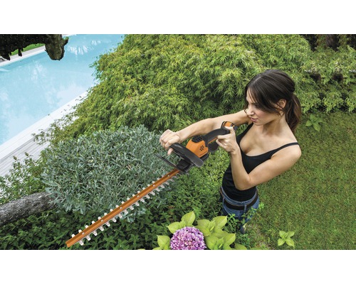 Frau schneidet Hecke mit einer Heckenschere im Garten.