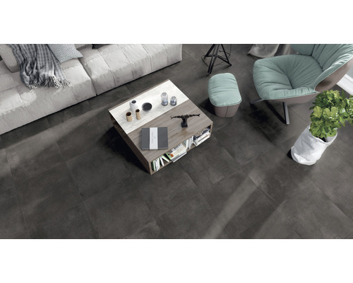 Wohnzimmer mit Couch, Sessel, Tisch und dunklen Bodenfliesen.