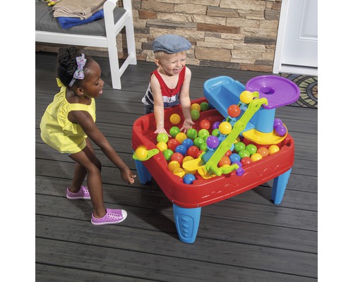 Kinder spielen mit einem Spieltisch mit Bällen im Garten.