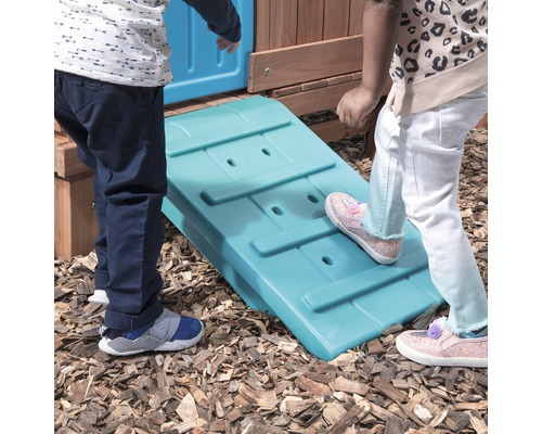 Kinder spielen auf einer Rampe an einem Spielhaus im Garten.