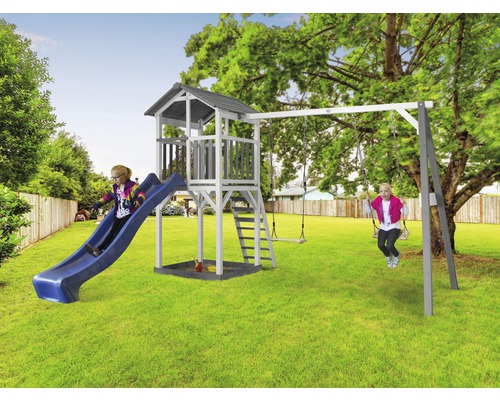 Kind auf einer Rutsche und Kind auf einer Schaukel an einem Spielturm mit Sandkasten im Garten.