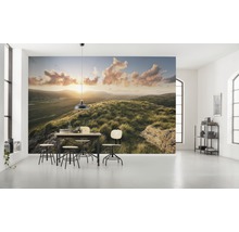 Helles Zimmer mit Fototapete einer Hügellandschaft bei Sonnenaufgang und Esstischgruppe