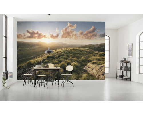Helles Zimmer mit Fototapete einer Hügellandschaft bei Sonnenaufgang und Esstischgruppe