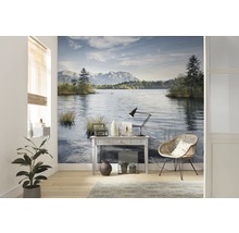 Wohnraum mit Wandtapete, die einen See und Berge zeigt, sowie einem Tisch, einer Lampe und einem Stuhl.