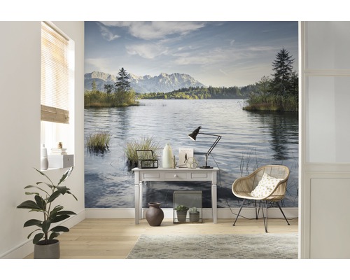 Wohnraum mit Wandtapete, die einen See und Berge zeigt, sowie einem Tisch, einer Lampe und einem Stuhl.