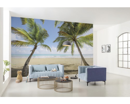 Wohnraum mit Fototapete, die eine tropische Szene mit Palmen und Strand zeigt, mit Möbeln wie Sofa und Sesseln.