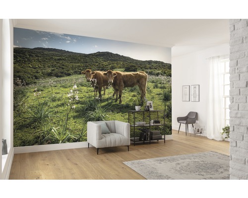 Wohnraum mit Fototapete mit Kühen auf einer Wiese vor einem bewaldeten Hügel