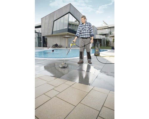 Ein Mann reinigt mit einem Hochdruckreiniger eine Terrasse neben einem Pool.