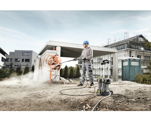Ein Mann reinigt mit einem Hochdruckreiniger einen Betonmischer auf einer Baustelle.