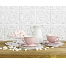 Dekorative Wand mit Reliefmuster, rosa Tassen, Milchkanne und Marshmallows auf einem Tisch.