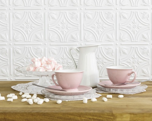 Dekorative Wand mit Reliefmuster, rosa Tassen, Milchkanne und Marshmallows auf einem Tisch.