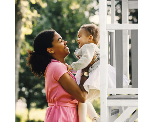 Mutter hält lachendes Kleinkind auf einer Spielstruktur im Garten